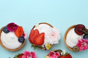 Sweet tartlets with berries and flowers on turquoise background, flat lay with space for text. Delicious dessert
