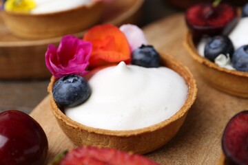 Sweet tartlets with berries and flowers on table, closeup. Delicious dessert