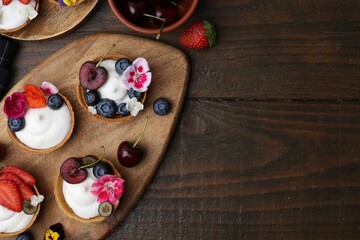 Sweet tartlets with berries and flowers on wooden table, flat lay with space for text. Delicious dessert
