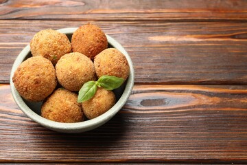 Delicious fried croquette balls with basil in bowl on wooden table, closeup. Space for text