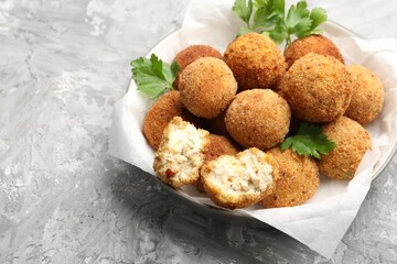 Delicious fried croquette balls with parsley in bowl on grey textured table, closeup. Space for text
