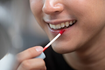 Beauty Care. Male applying red lip gloss with a smile.