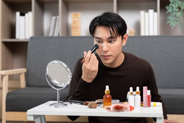 Makeup Application. Young man using brush to apply foundation in front of mirror.