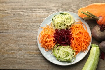 Different noodles and vegetables on wooden table, flat lay. Space for text
