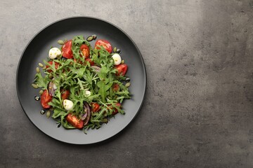 Tasty salad with arugula, mozzarella and vegetables on grey table, top view. Space for text