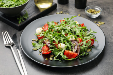 Tasty salad with arugula, mozzarella and vegetables served on grey table, closeup