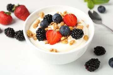 Tasty yogurt with granola and berries in bowl on white table, closeup