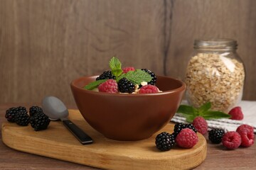 Tasty yogurt with granola and berries in bowl on wooden table, closeup