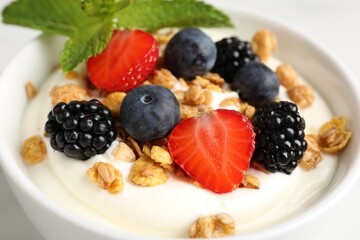 Tasty yogurt with granola and berries in bowl on white table, closeup