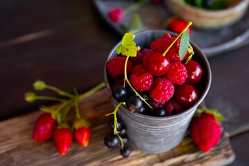  Different types of berries on a black wooden background. Raspberry, strawberry, cherry and currant close up
