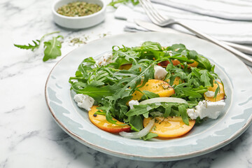 Tasty salad with arugula, cheese, peach, basil and spices on white marble table, closeup