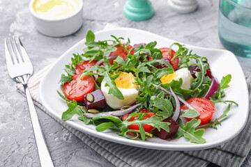 Tasty salad with arugula, vegetables and egg served on grey table, closeup