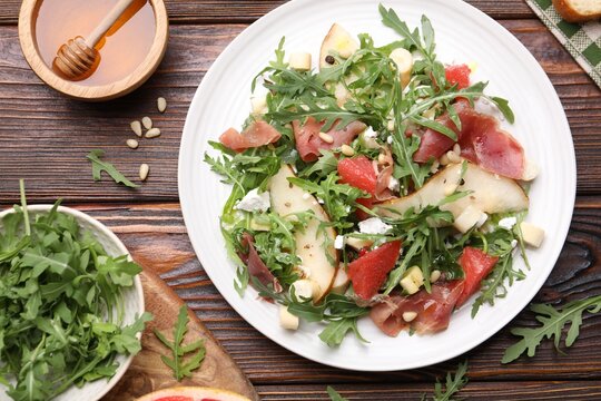 Tasty salad with arugula and prosciutto served on wooden table, flat lay - Powered by Adobe