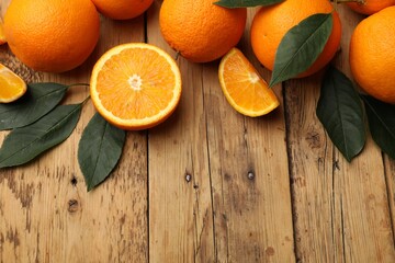 Fresh ripe oranges and leaves on wooden table, flat lay. Space for text