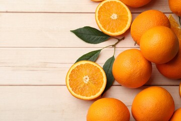 Fresh ripe oranges and leaves on light wooden table, flat lay. Space for text