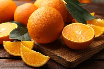 Fresh ripe oranges and leaves on wooden table, closeup