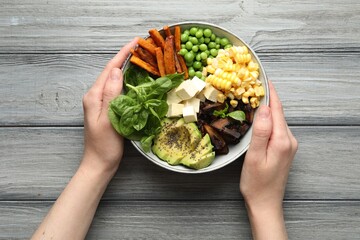 Healthy vegetarian food. Woman with delicious Buddha bowl at grey wooden table, top view
