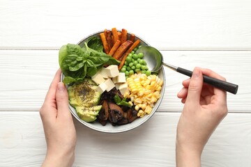 Healthy vegetarian food. Woman eating delicious Buddha bowl at white wooden table, top view