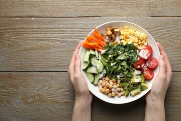 Woman with different healthy vegetarian food at wooden table, top view. Space for text