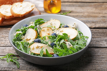 Tasty salad with arugula, pear, blue cheese, peanuts and blueberries in bowl on wooden table, closeup