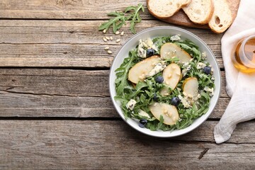 Tasty salad with arugula, pear, blue cheese, peanuts and blueberries in bowl on wooden table, flat lay. Space for text
