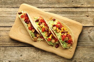 Tasty vegetarian tacos with beans, tofu and vegetables on wooden table, top view