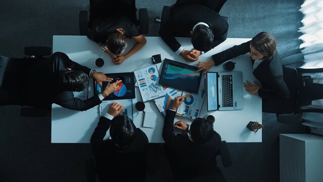 Top down aerial view of professional businessman handed out financial statistic to analyst data investment graph. Group of diverse investors brainstorming and planning marketing strategy. Directorate.