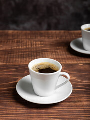 Two white cups of dark coffee sit on a rich brown wooden table.