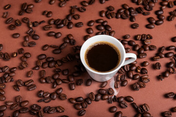 A espresso cup filled with dark coffee surrounded by roasted beans on reflective surface.