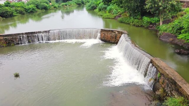 Flowing water over rural check dam in lush green Indian landscape during monsoon &ndash; ideal for nature, agriculture, environment, eco-tourism, and countryside themes.