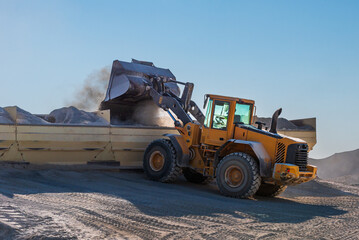 Wheel loader at an asphalt plant filling storage bins with different types of sand for asphalt production.