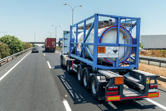 Truck with a tank container carrying titanium tetrachloride, marked with toxic and corrosive hazard placards and an 'X' indicating water-reactive substance.