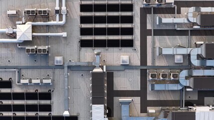Top-down aerial view of a commercial rooftop featuring solar panels, HVAC ducts, vents, and cooling units on a flat concrete surface. - Powered by Adobe