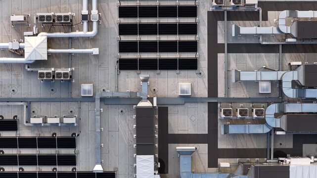 Top-down aerial view of a commercial rooftop featuring solar panels, HVAC ducts, vents, and cooling units on a flat concrete surface. - Powered by Adobe