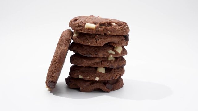 Stacked cookies with individual pieces visible. A stack of cookies rotates vertically, while the front cookie stands alone. The white chocolate pieces are particularly visible.