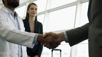 Doctor and businessman shaking hands in airport for medical partnership. - Powered by Adobe