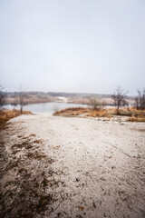 dirty beach with sand, near a calm lake covered with a light fog