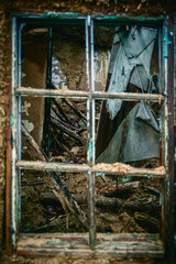 An old broken wooden window frame in a clay house, through which the ruined interior of the house can be seen