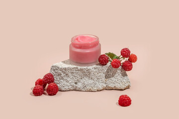 A jar of natural body scrub on a stone podium and raspberry berries on a beige background