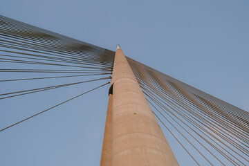Upward view of modern cable-stayed bridge with geometric lines and clear sky, minimal architectural...
