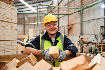 Smiling warehouse worker wearing safety vest and helmet holding a timber block in pallet facility, showcasing positive workplace energy and timber sorting process in progress.