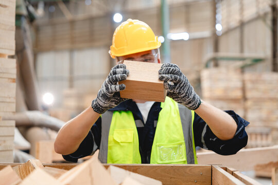 Close-up of focused industrial worker holding wooden block with both hands for visual inspection inside pallet logistics warehouse, aiming to meet construction and freight handling standards.