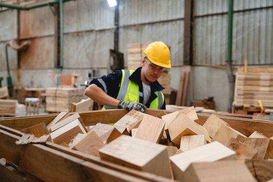 Male staff member enjoying timber work, holding a square wooden piece inside production warehouse, contributing to pallet material preparation and sustainable reuse planning.
