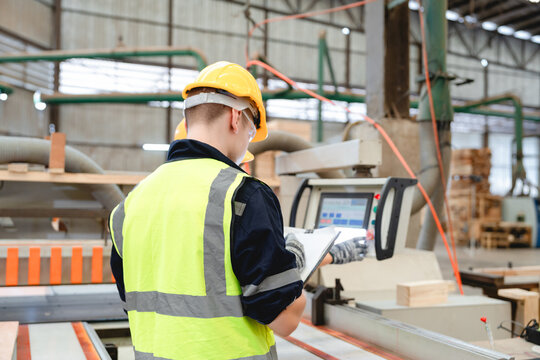 Back view of factory technician managing electronic interface of machinery in timber workshop, recording performance data and overseeing automated functions. - Powered by Adobe