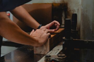Close-up image of male worker's hands positioning wooden plank into cutting machine at timber factory