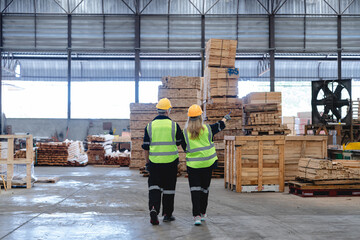 Fototapeta premium Two warehouse employees inspecting wooden pallets in lumber facility. The female staff is pointing at stacked wood while holding clipboard. The male colleague listens attentively.