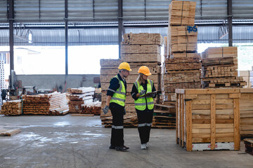Fototapeta premium Male and female factory staff walking together through lumber storage area, discussing material management in organized industrial environment, captured in wide-angle shot. 