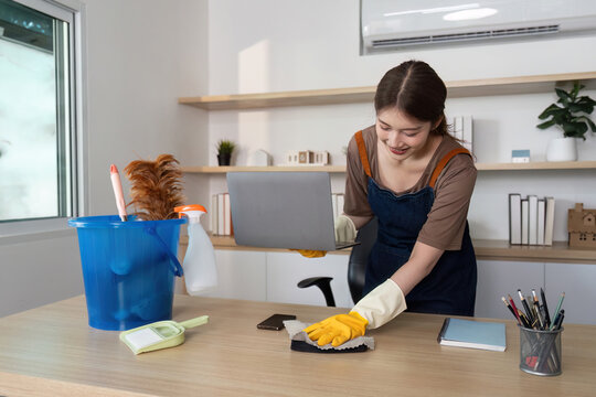 Home Cleaning. Young woman happily organizing her workspace while cleaning.