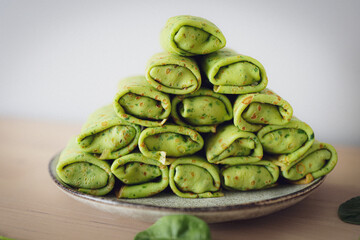 Thin spinach crepes neatly rolled and stacked on a plate, showcasing their vibrant green color and fresh ingredients