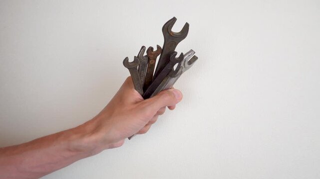 The hand holds a set of wrenches of different sizes against the background of a light wall. A close-up is a tool for repair and maintenance. Close-up of a man's hand holding a monkey wrench.